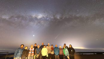 A group poses in front of of a starry sky with a visible comet